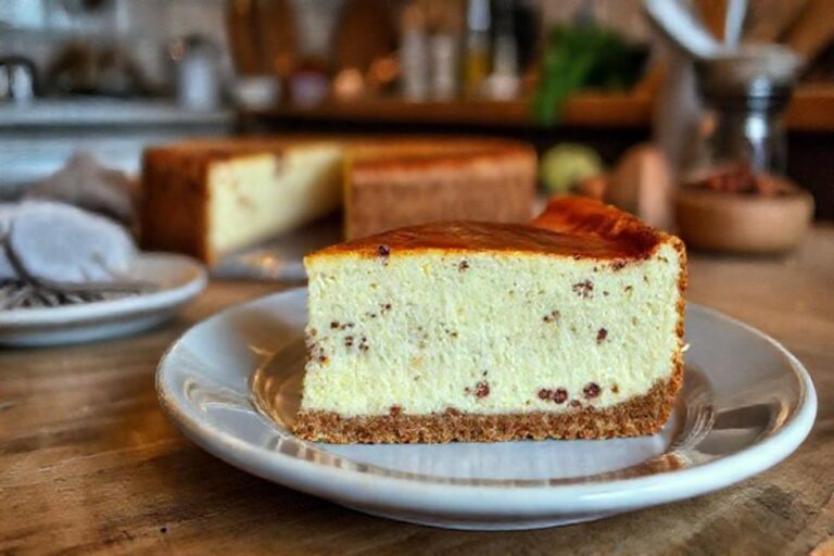 Uma fatia de cheesecake basca em um prato com um ambiente aconchegante ao fundo.